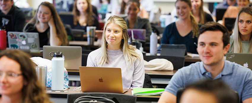 Students sitting in classroom with their laptops.