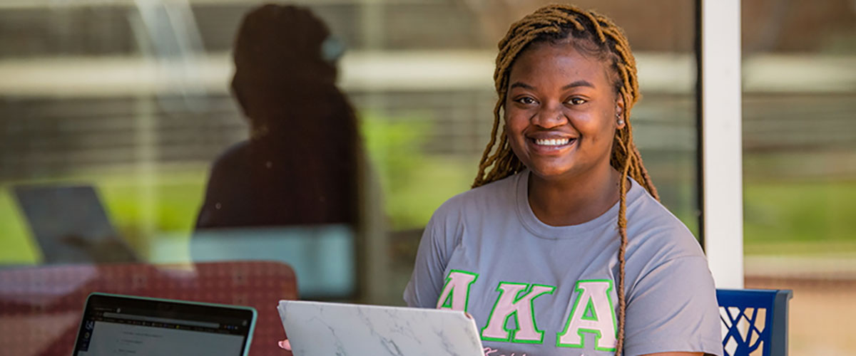 Female student sitting outside at a table working on a laptop.