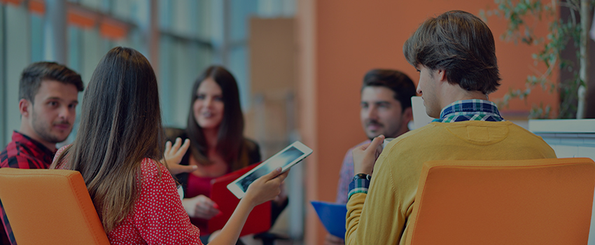 Group of people sitting in a circle talking with one holding a tablet.