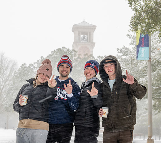 Students on campus during snow day holding up J hand for Jaguars.