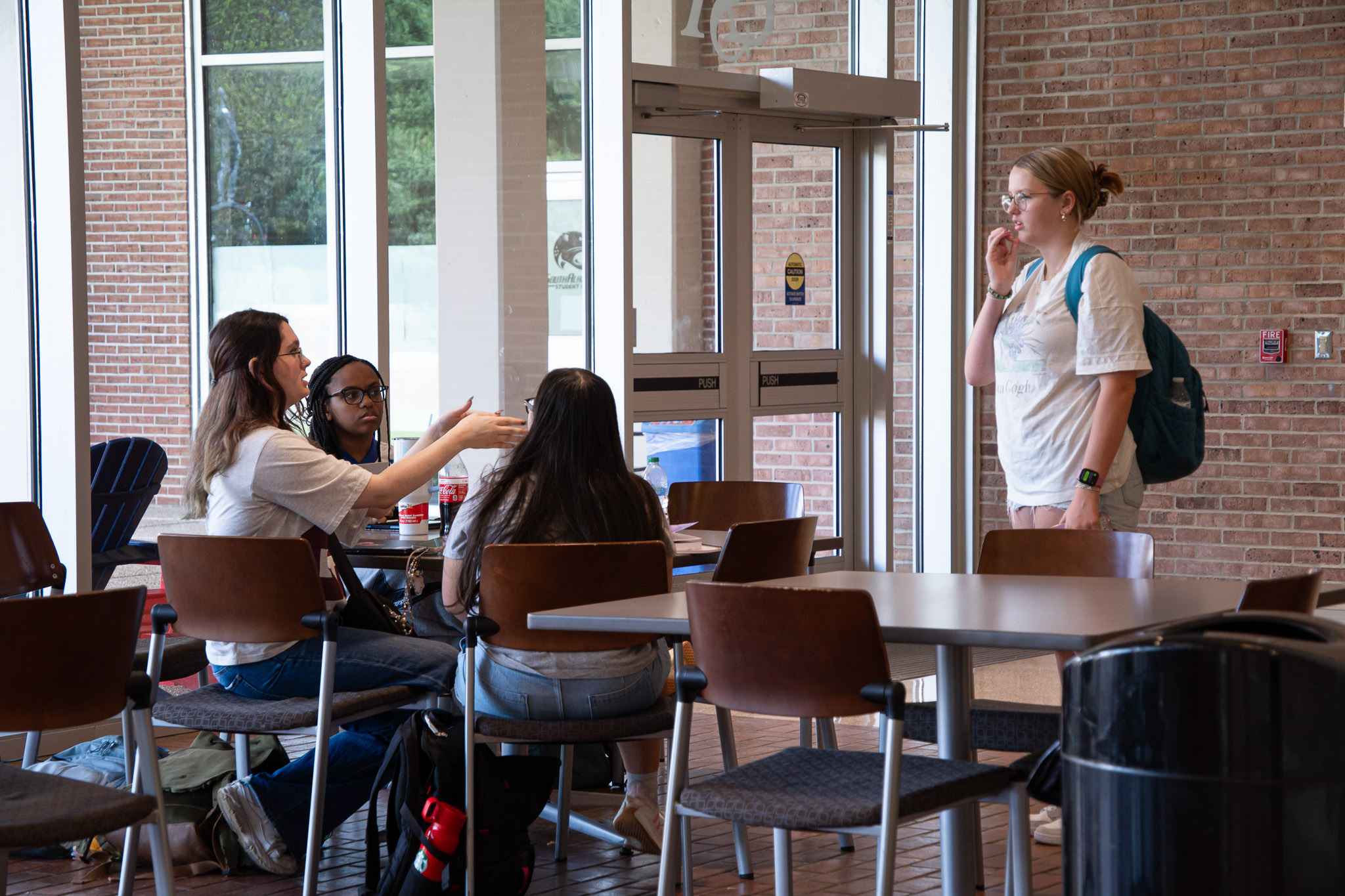 students sitting at table and talking with student standing